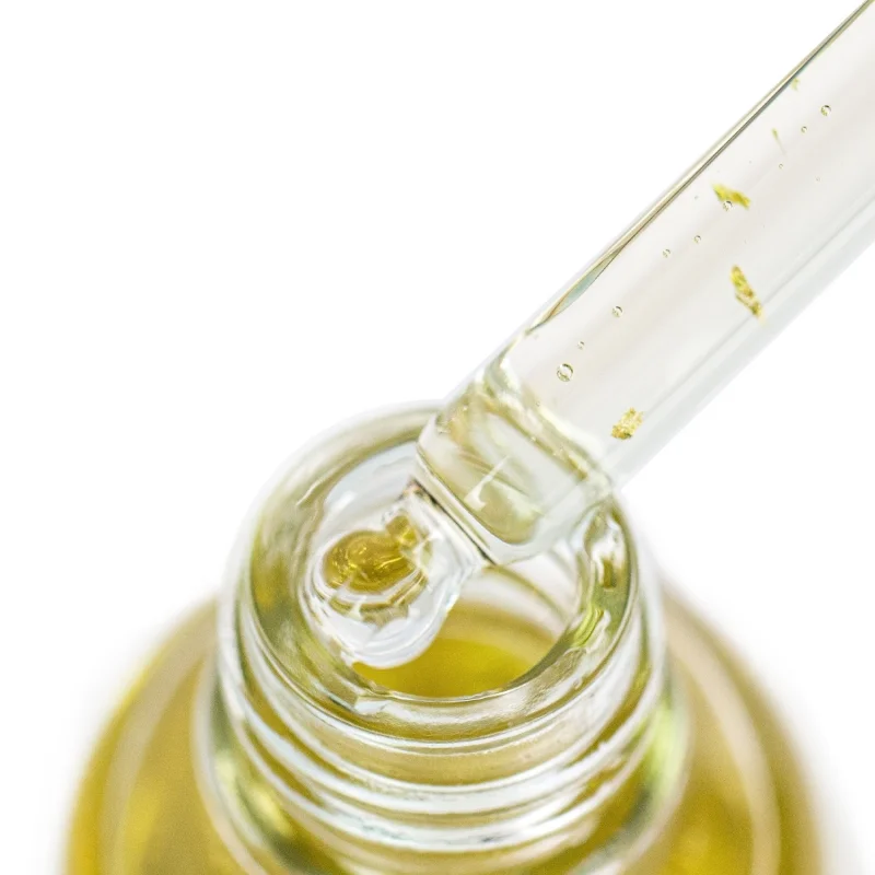 Makro pipety z płatkami złota nad szyjką butelki Yokaba 24k Gold Care Oil
