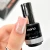 Elarto Lakier do stempli Stamp Nail Polish 03 Silver 7 ml - paznokieć w odcieniu nude z odbitym srebrnym wzorem kwiatów, obok butelka lakieru w dłoni