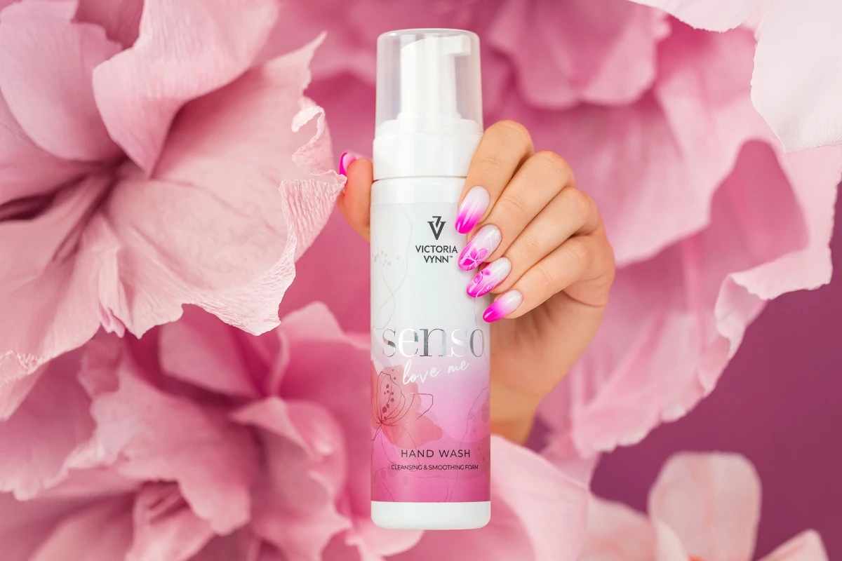 Butelka pianki SENSO Love Me 200 ml w dłoni ze stylizacją ombré, w tle różowe kwiaty