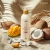 Butelka kremu Yokaba Mango&Coco 240 ml na piasku, obok kokosy, mango i cień liścia palmy