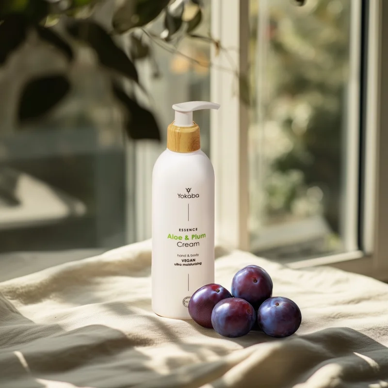 Butelka kremu Yokaba Aloe&Plum 240 ml na lnianej tkaninie w świetle okna, obok śliwki