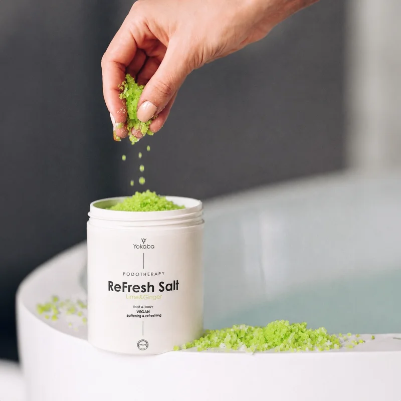 Dłoń wsypująca zieloną sól Yokaba ReFresh Salt Lime & Ginger do kąpieli stóp