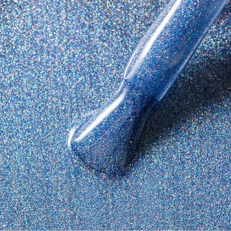 Elarto Top kocie oko i holo w jednym Catlight Denim 7ml - zbliżenie pędzelka z niebieskim topem pełnym holograficznych drobin na tle w tym samym odcieniu