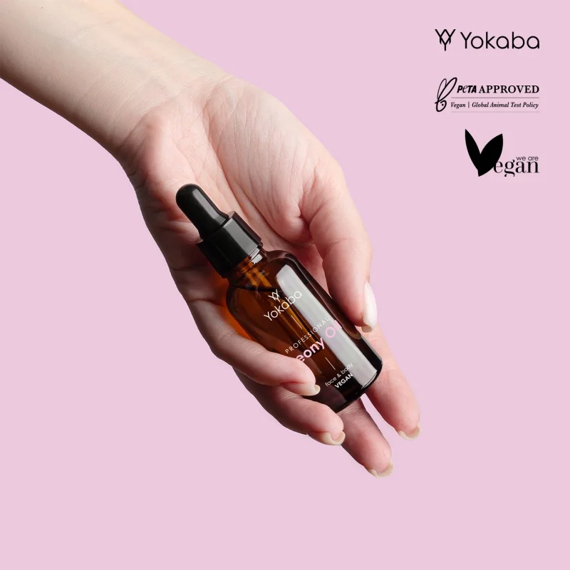 Butelka olejku Yokaba Peony Oil trzymana w otwartej dłoni na różowym tle, obok oznaczenia vegan i PETA approved