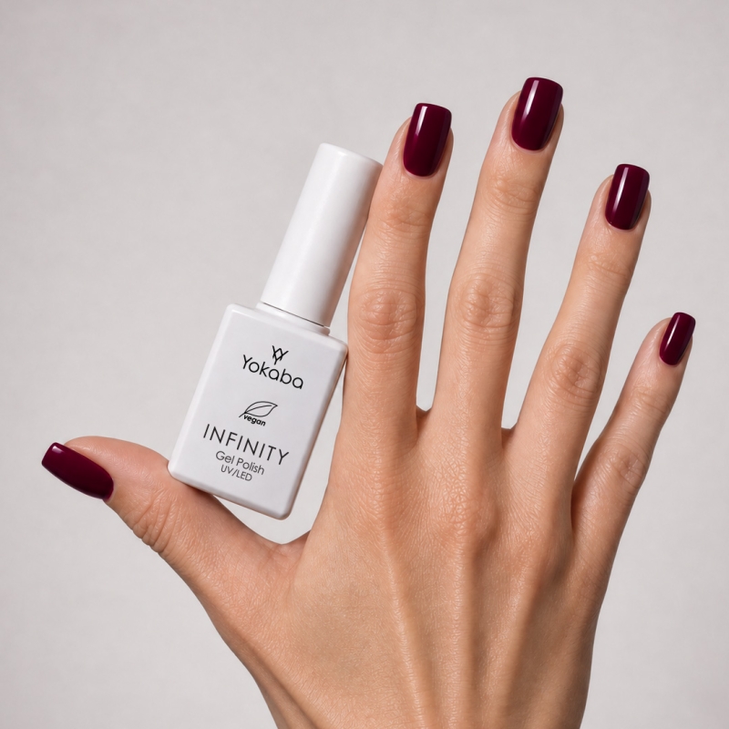 Lakier hybrydowy Yokaba Infinity 20 Black Cherry na paznokciach, dłoń z butelką